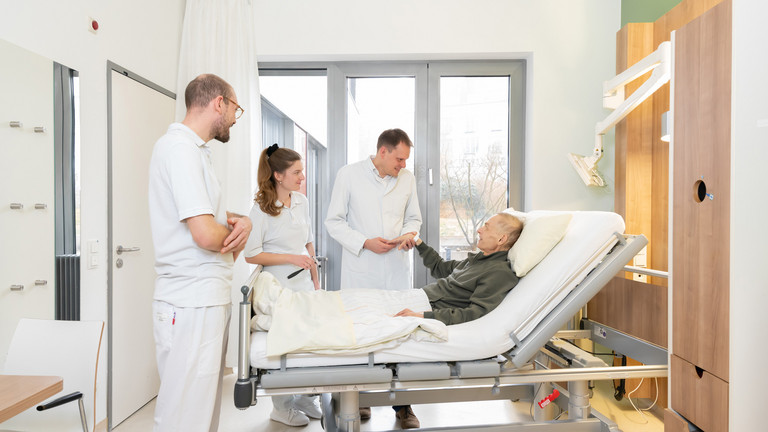 Prof. Kamp mit zwei Studierenden am Bett eines Palliativpatienten