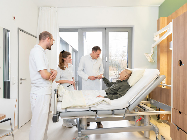 Prof. Kamp mit zwei Studierenden am Bett eines Palliativpatienten