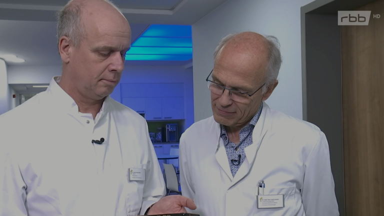 Dr. Hans-Josef Lemmen und Dr. Marko Böhm blicken im Krankenhausflur auf ein Smartphone im Immanuel Universitätsklinik Rüdersdorf