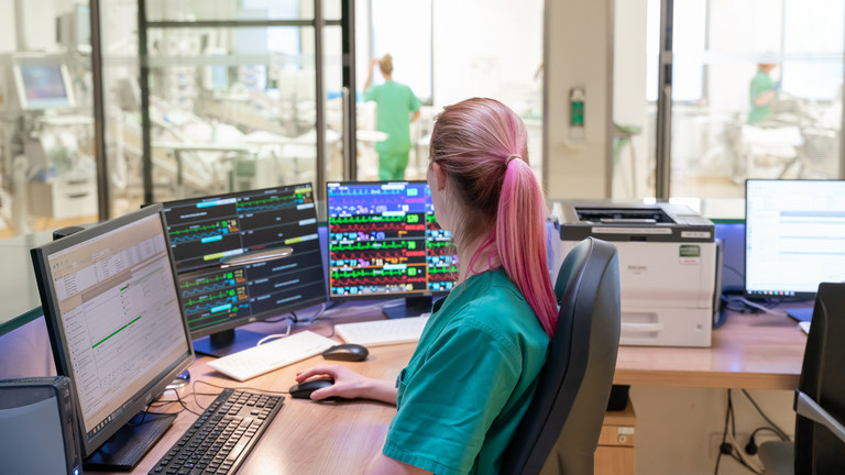 Pflegekraft an Arbeitsplatz mit mehreren Monitoren Pflegekraft an Arbeitsplatz mit mehreren Monitoren